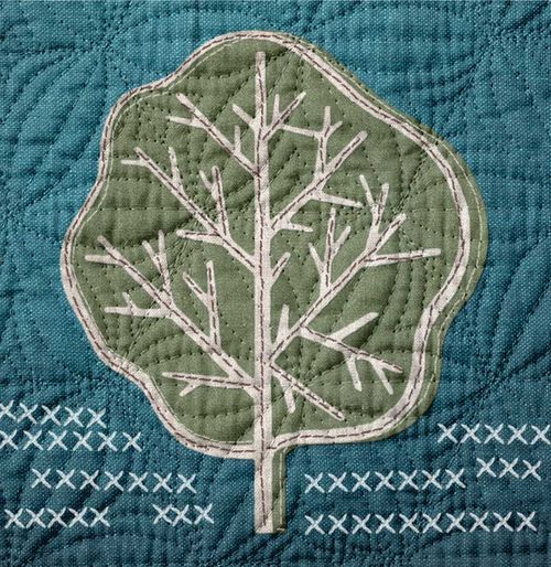A blue quilt with a green and white tree pattern sewn into the fibers.